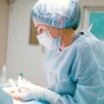 Female medical professional in surgical attire operating in a sterile room, focusing on patient care.